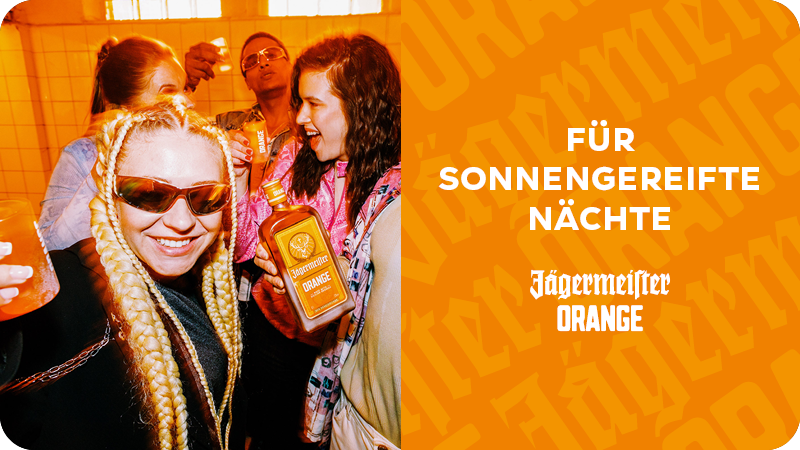 Ein Gruppe von Personen, die im Kreist steht, stößt mit einer Jägermeister Orange Flasche und Shotgläsern an