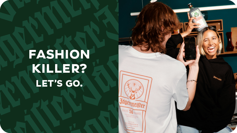 Im Vorgrund steht eine angerissene Flasche Jägermeister Manifest und im Hintergrund ist der untere Teil einer Person mit Jeans und Lederschuhen zu sehen